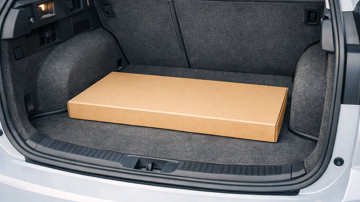 Flat-pack box placed inside a car trunk to check usable cargo width between the wheel arches